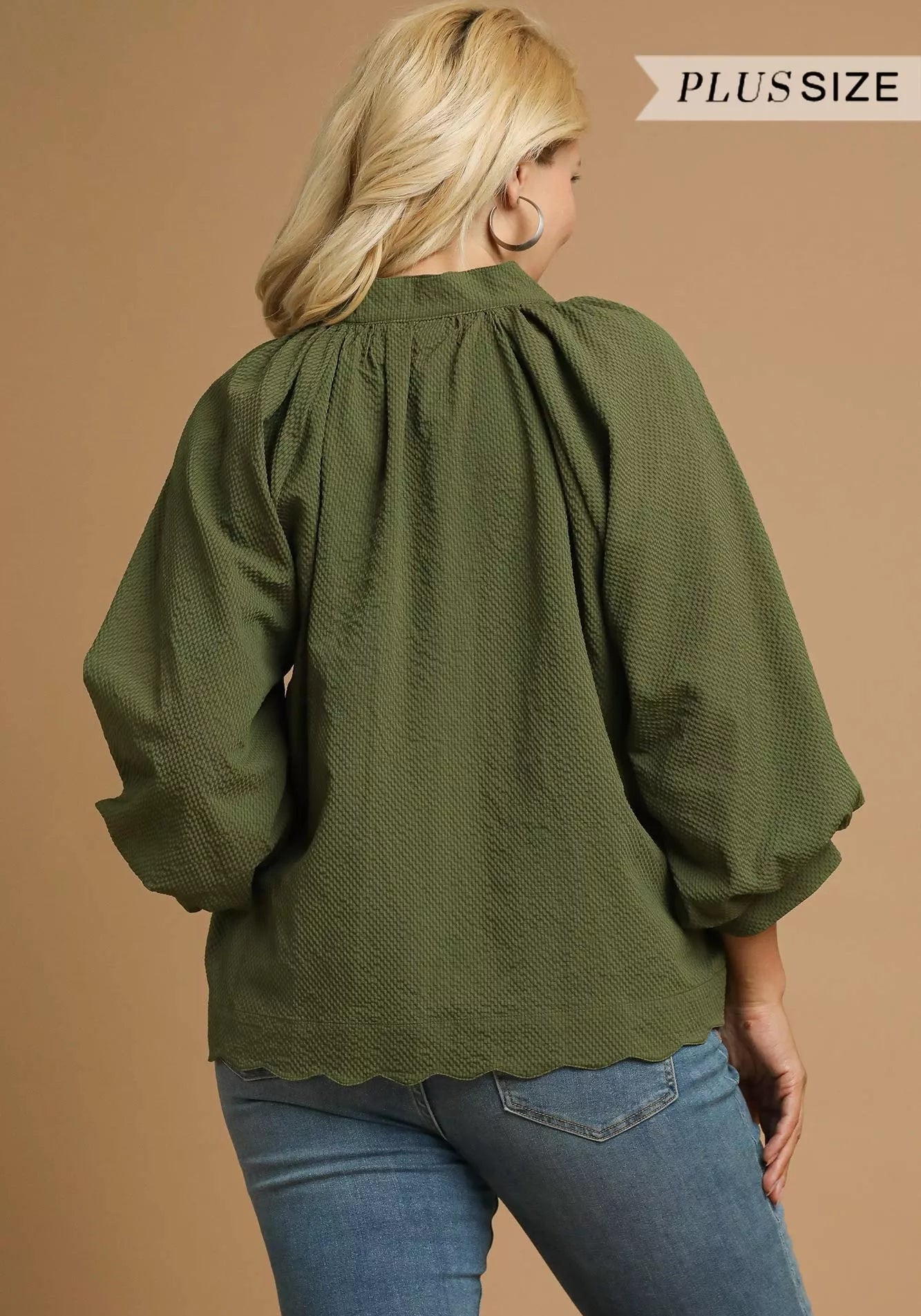 Person wearing an olive green blouse and blue jeans on a beige background