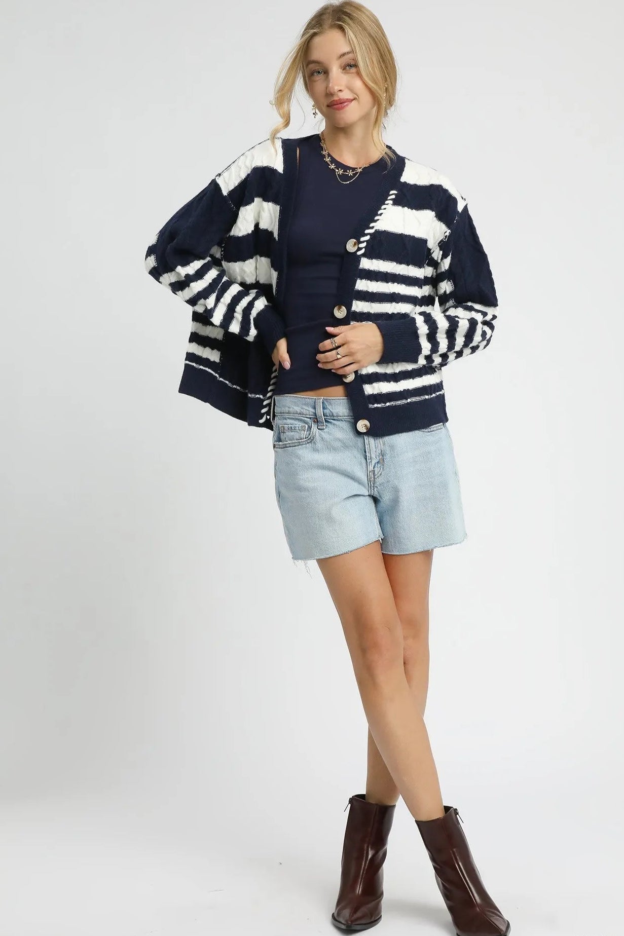 Woman wearing a navy and white striped cardigan with denim shorts and brown boots on a white background