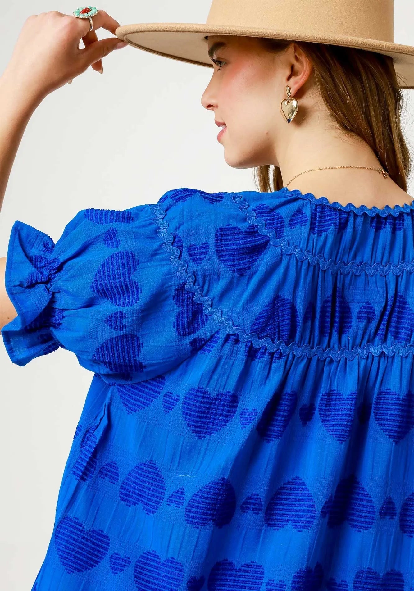 Woman wearing a blue dress with heart patterns and a beige hat against a neutral background