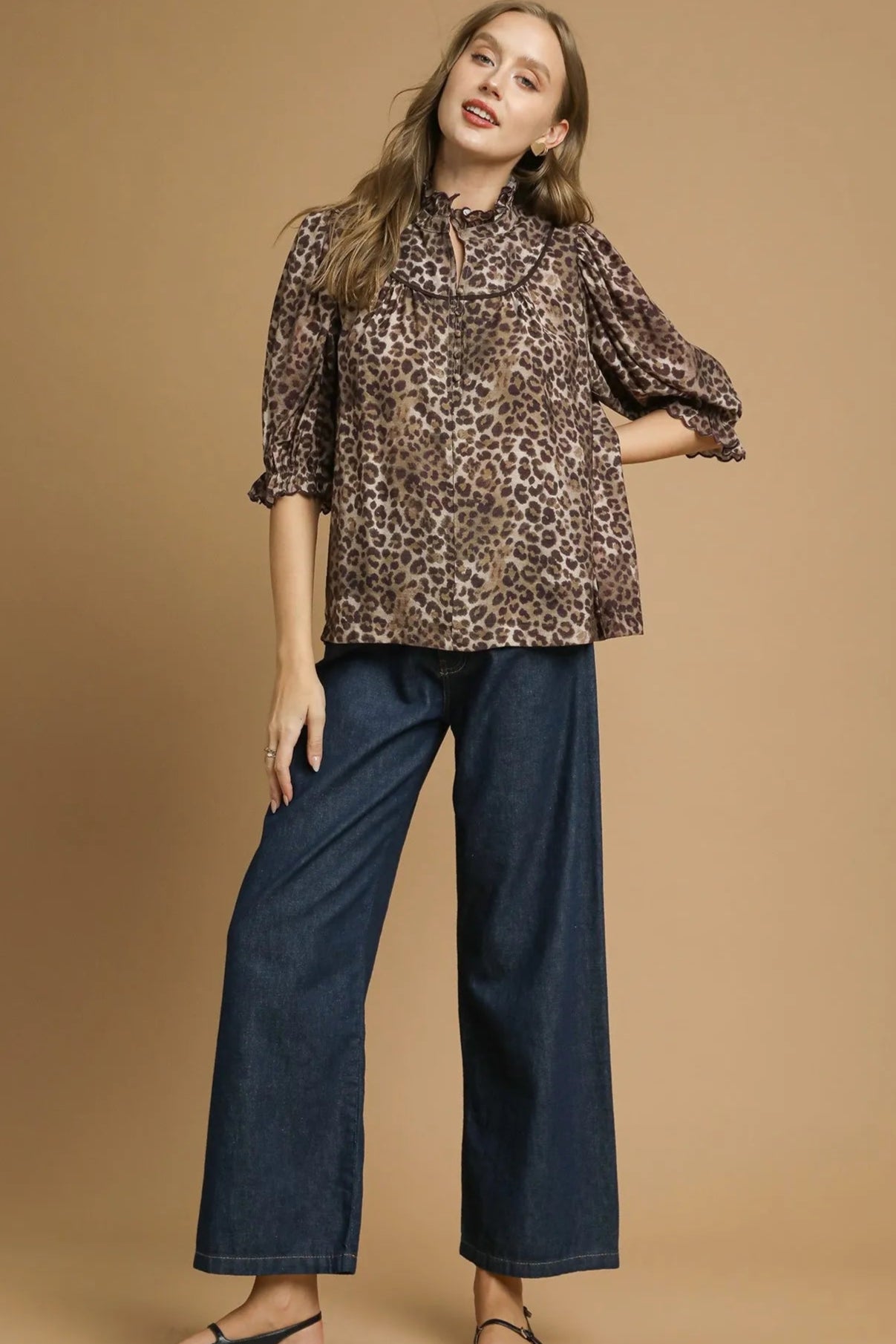 Woman wearing a leopard print top and blue pants on a beige background