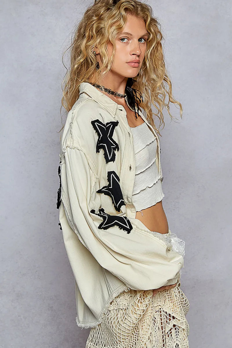 Woman wearing a white jacket with black star designs on a plain background