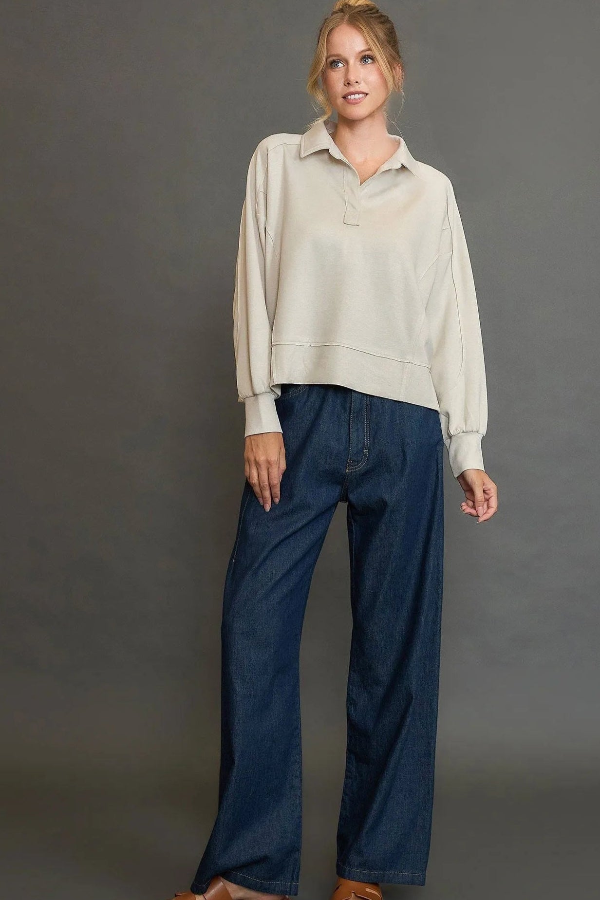 Woman wearing a light-colored top and blue pants against a gray background