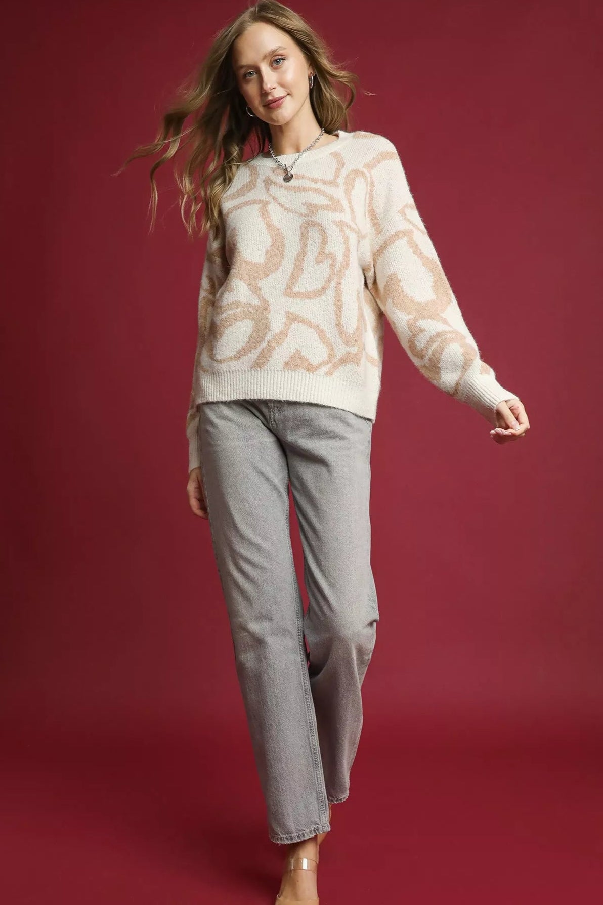 Woman wearing a patterned sweater and gray pants on a red background