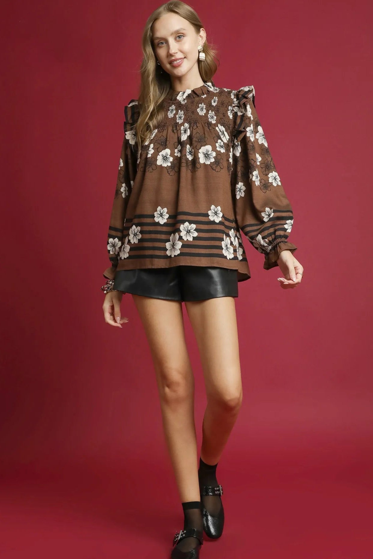 Woman wearing a brown floral blouse and black shorts on a red background