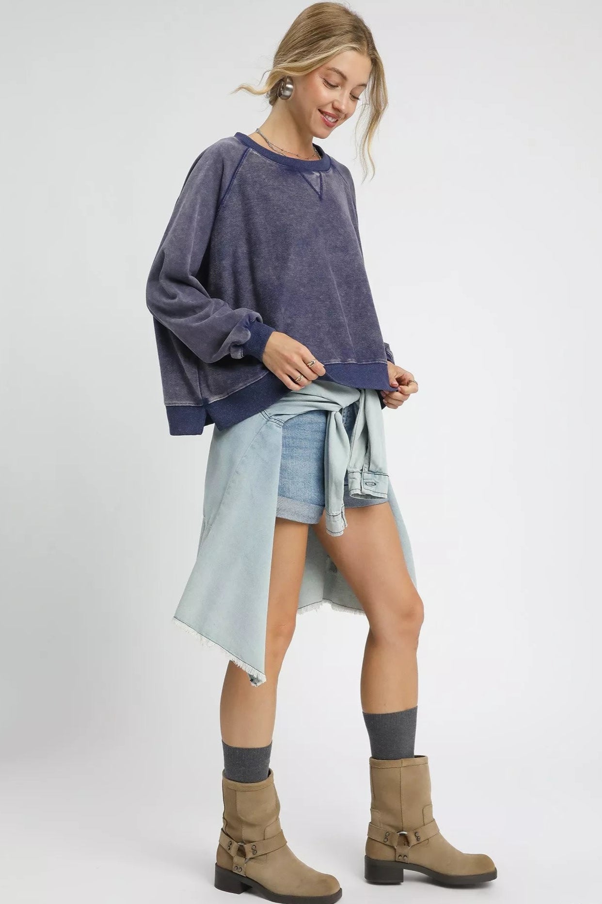 Woman wearing a navy sweater, denim shorts, and brown boots on a white background