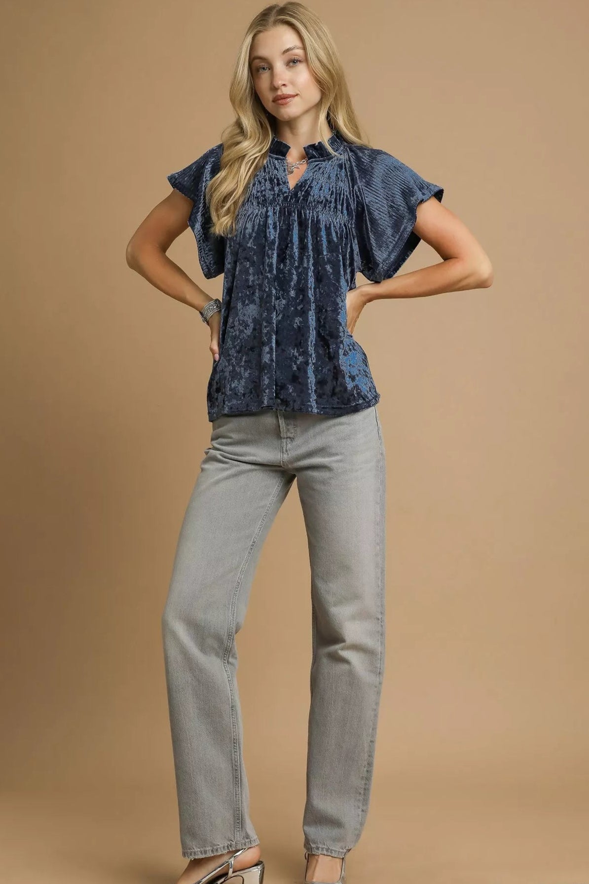 Woman wearing a blue velvet top and gray jeans on a beige background