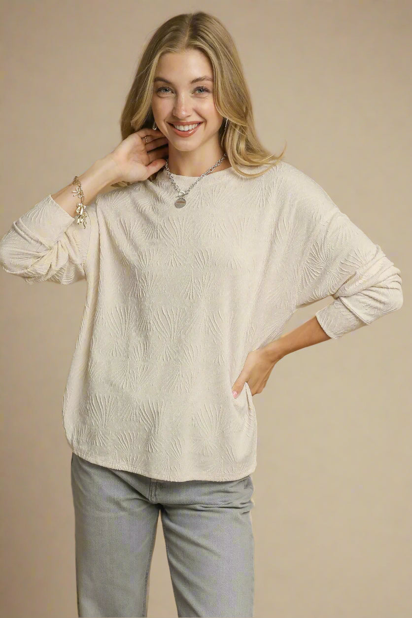 Woman wearing a beige sweater and gray pants against a brown background