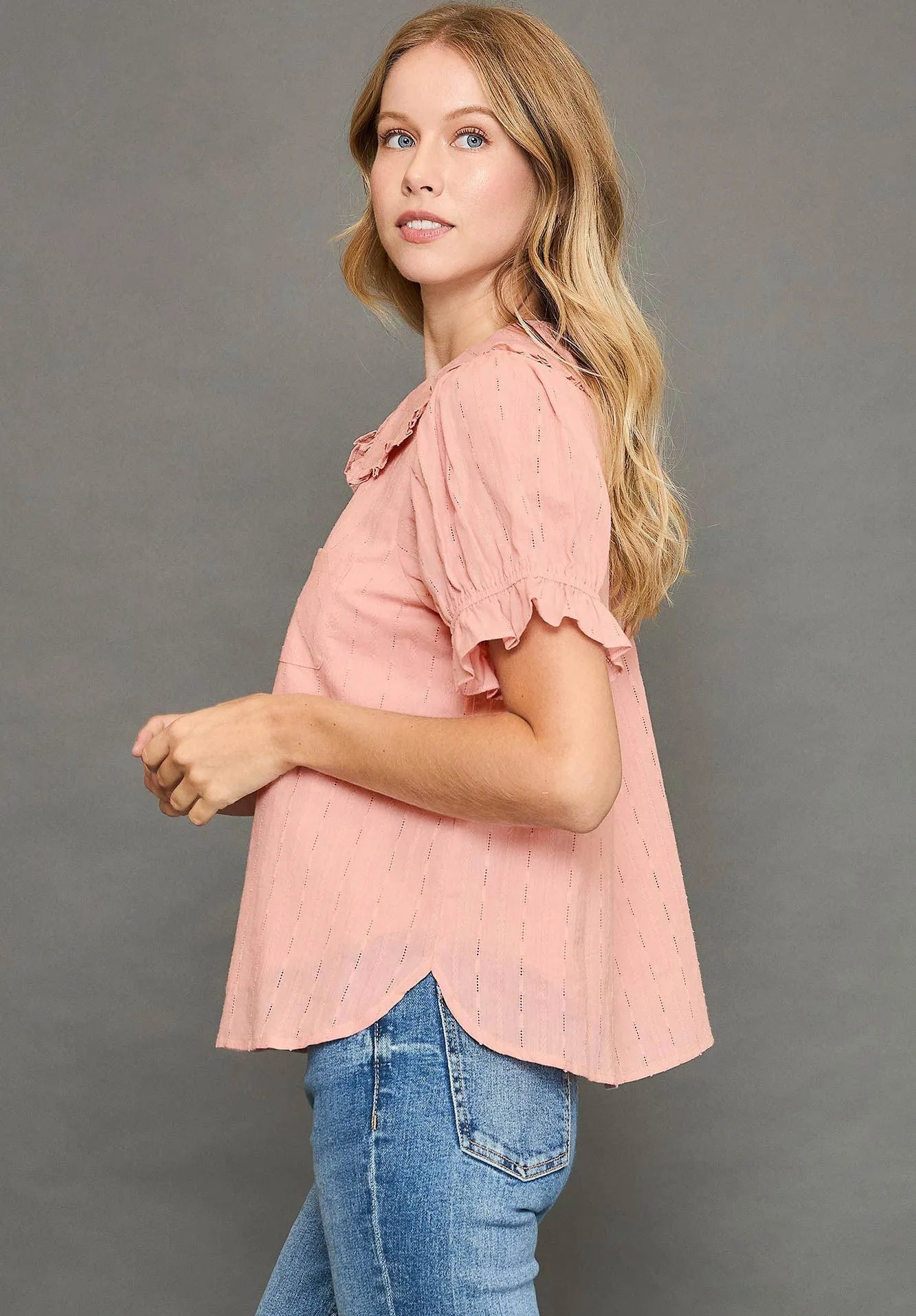 Woman wearing a pink blouse and blue jeans against a gray background