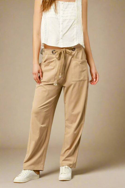 Person wearing beige pants with a white top on a gray background