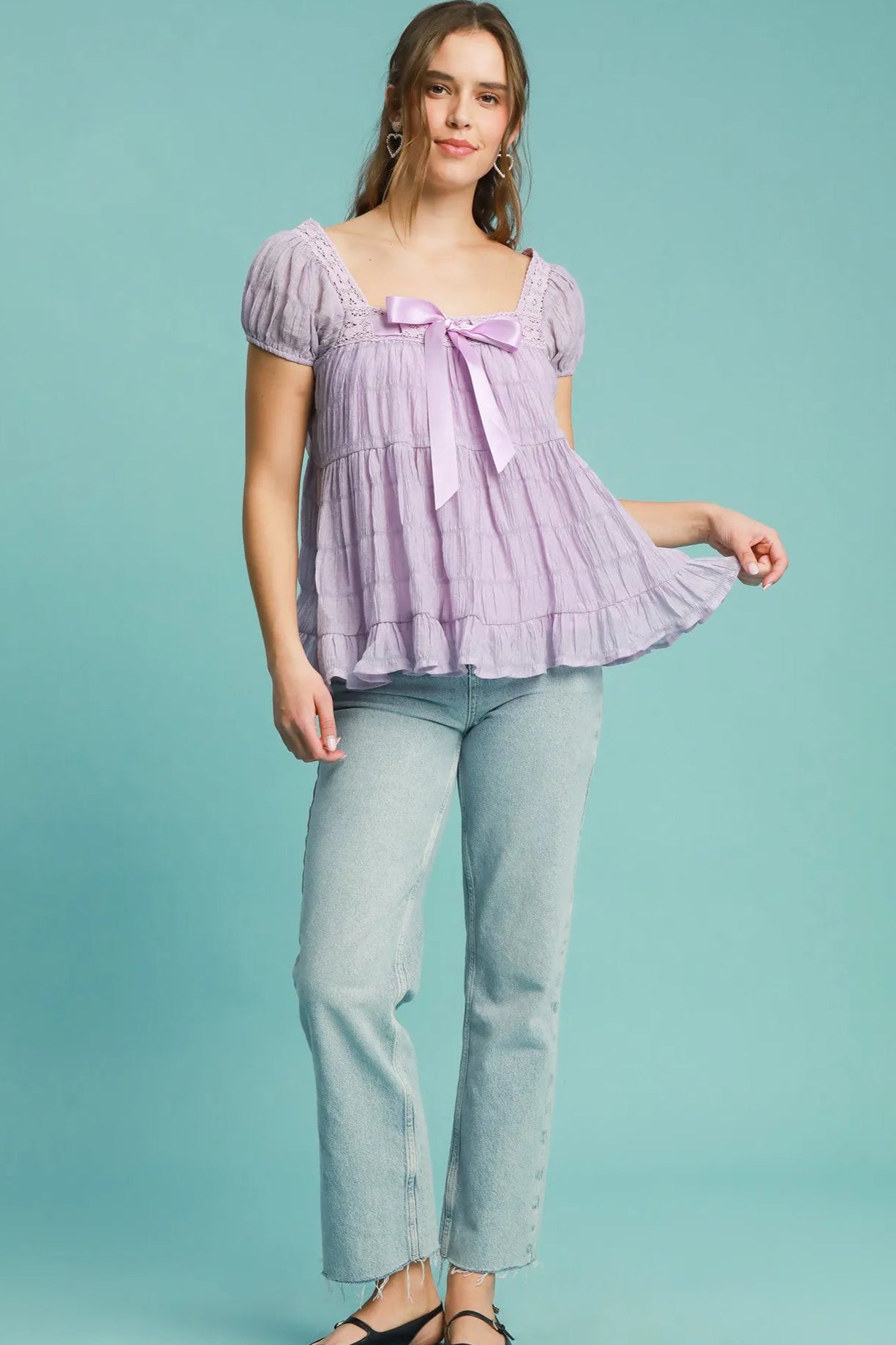 Woman wearing a lavender top with a bow and light blue pants on a teal background