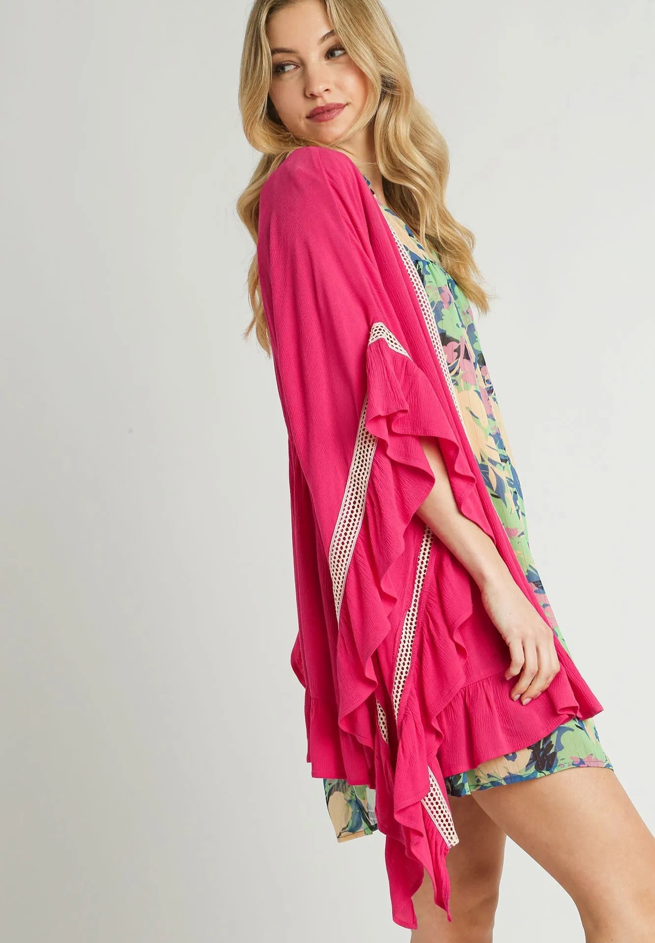 Woman wearing a pink kimono-style garment over a floral dress on a light gray background