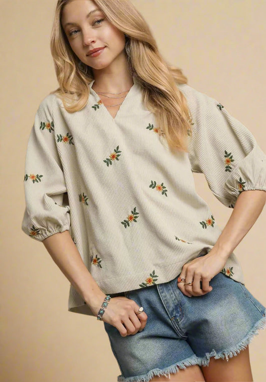 Woman wearing a cream blouse with floral patterns and denim shorts on a beige background