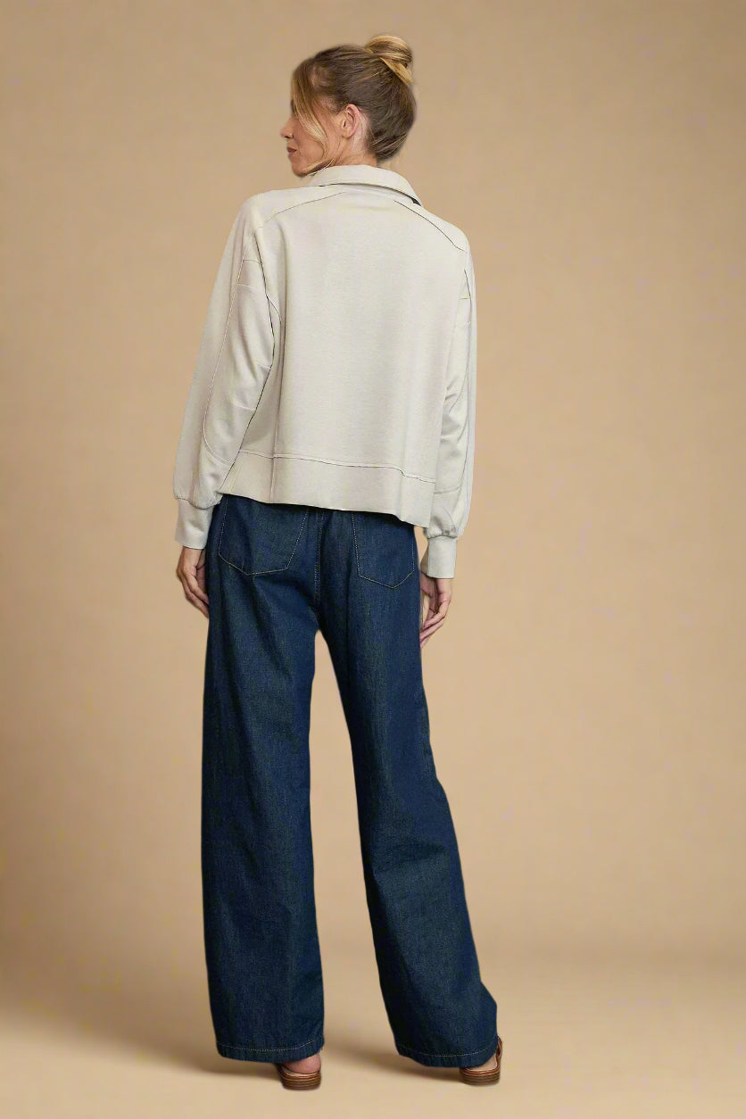 Person wearing a light-colored jacket and dark blue jeans against a gray background