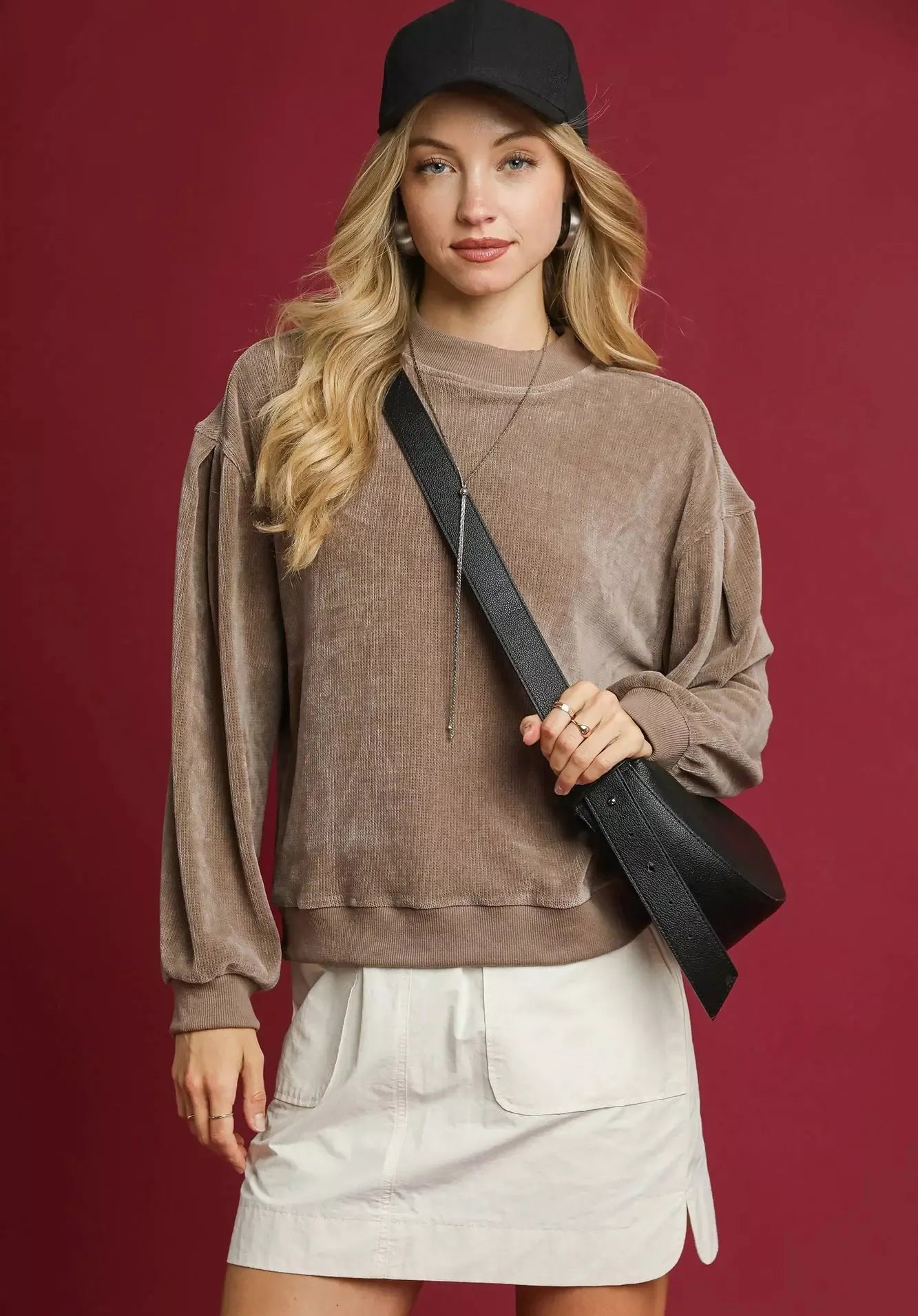 Woman wearing a brown sweater and white skirt with a black cap against a red background