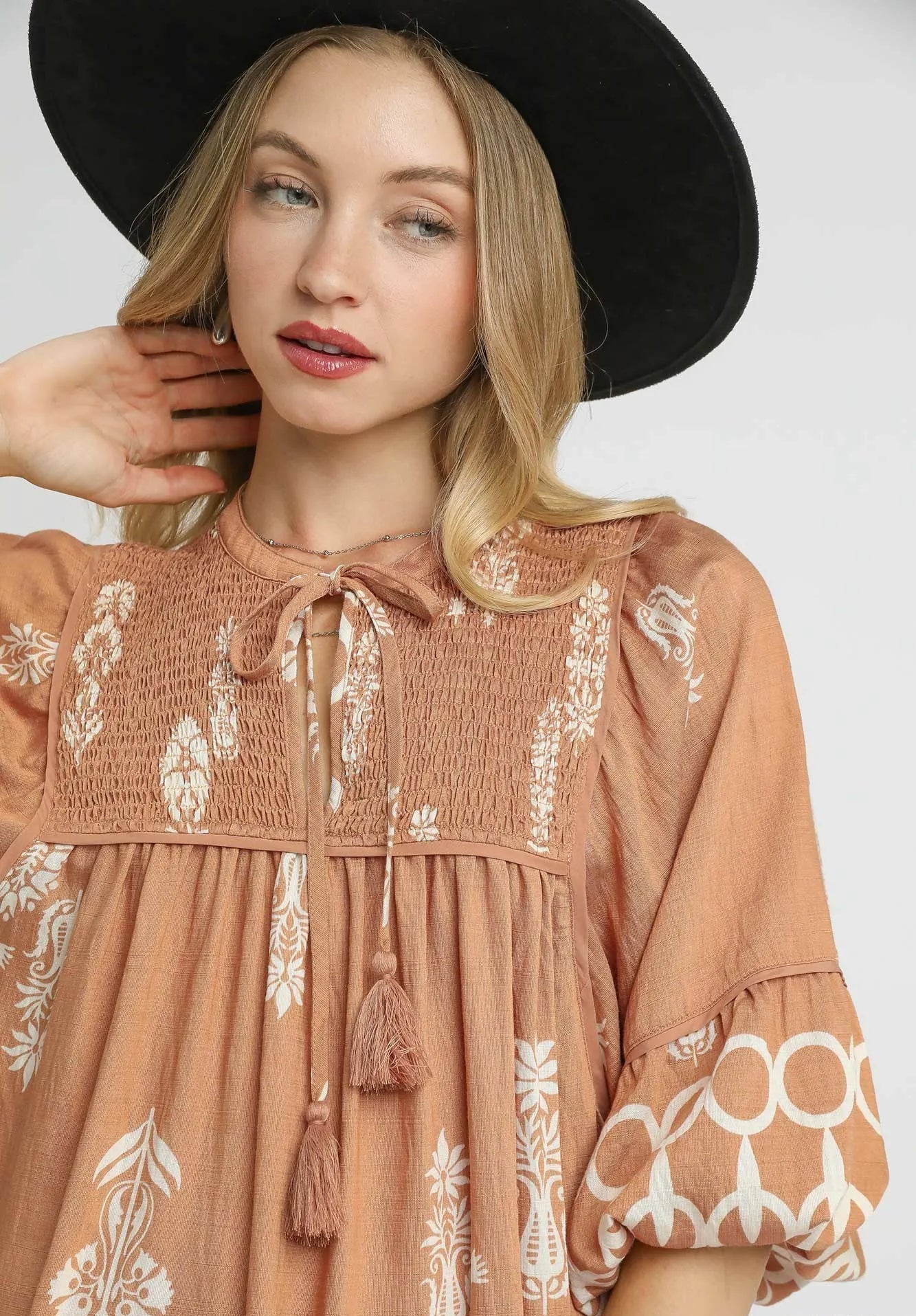Woman wearing a brown dress with white patterns and a black hat on a white background