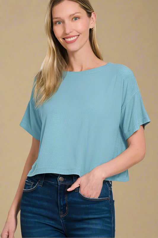 Woman wearing a dusty teal top and blue jeans on a white background