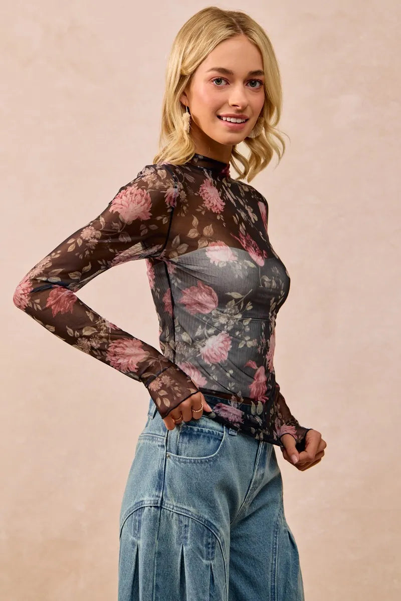 Woman wearing a floral sheer top and jeans against a beige background