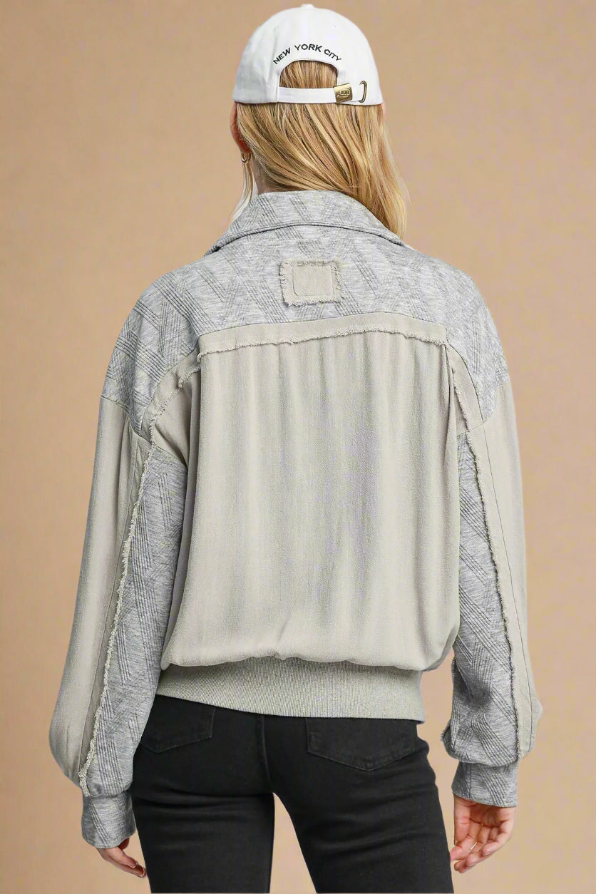 Person wearing a gray and beige jacket with a white cap on a plain background