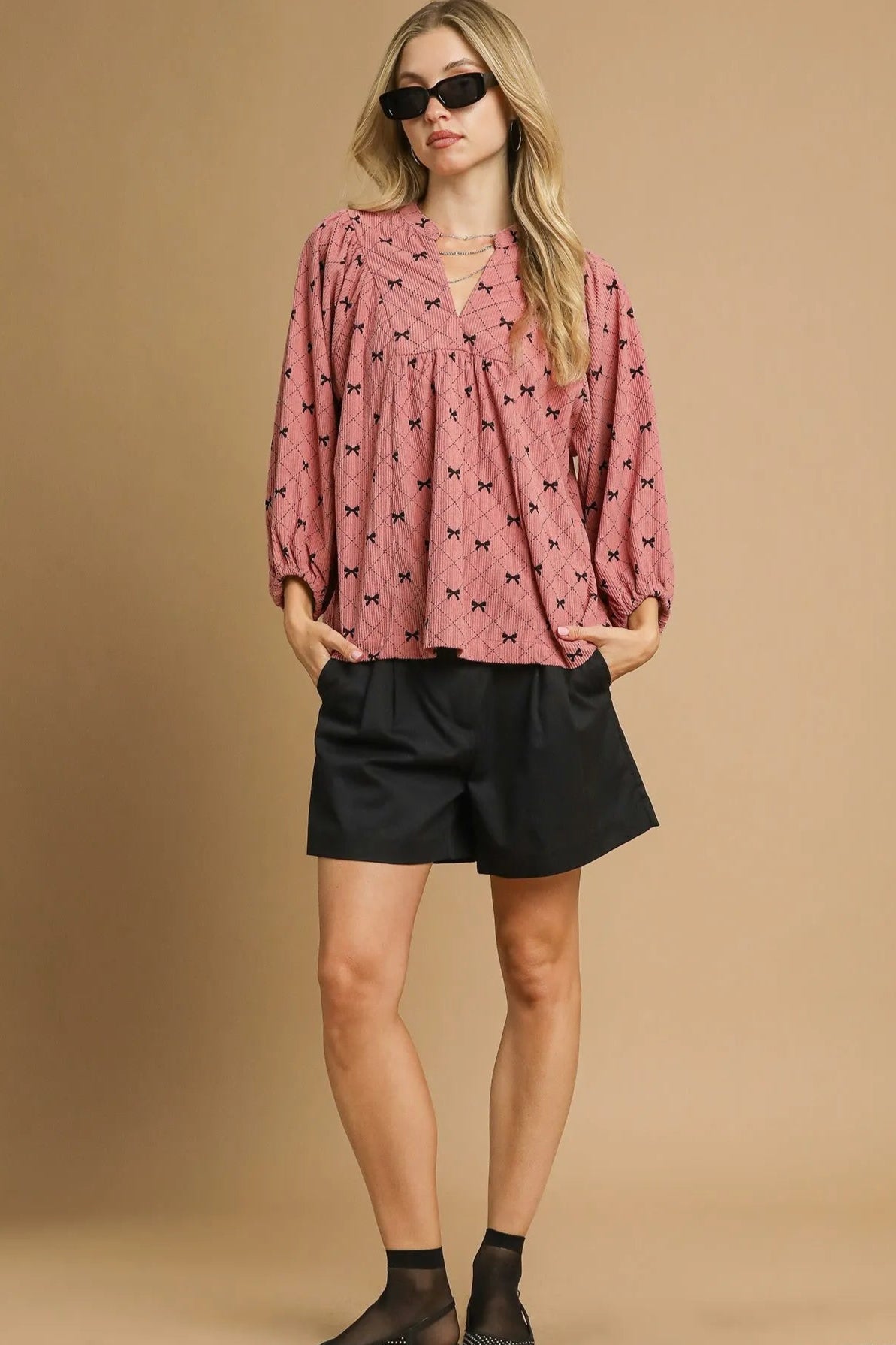 Woman wearing a pink blouse with black patterns and black shorts on a beige background