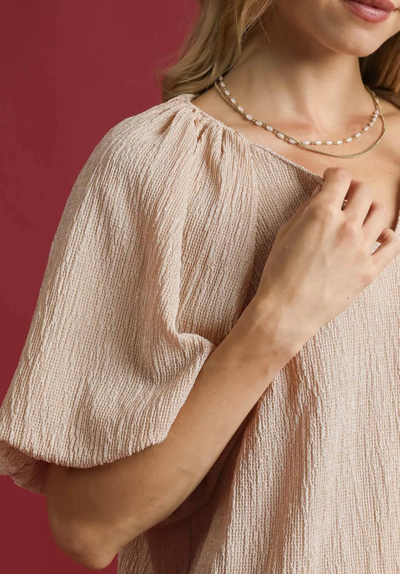 Woman wearing a beige top and pearl necklace against a red background