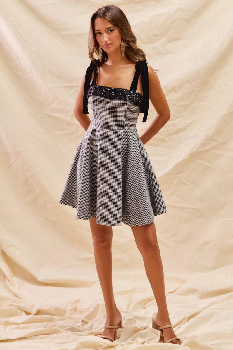 Woman wearing a black and white checkered dress with a bow detail on a beige background