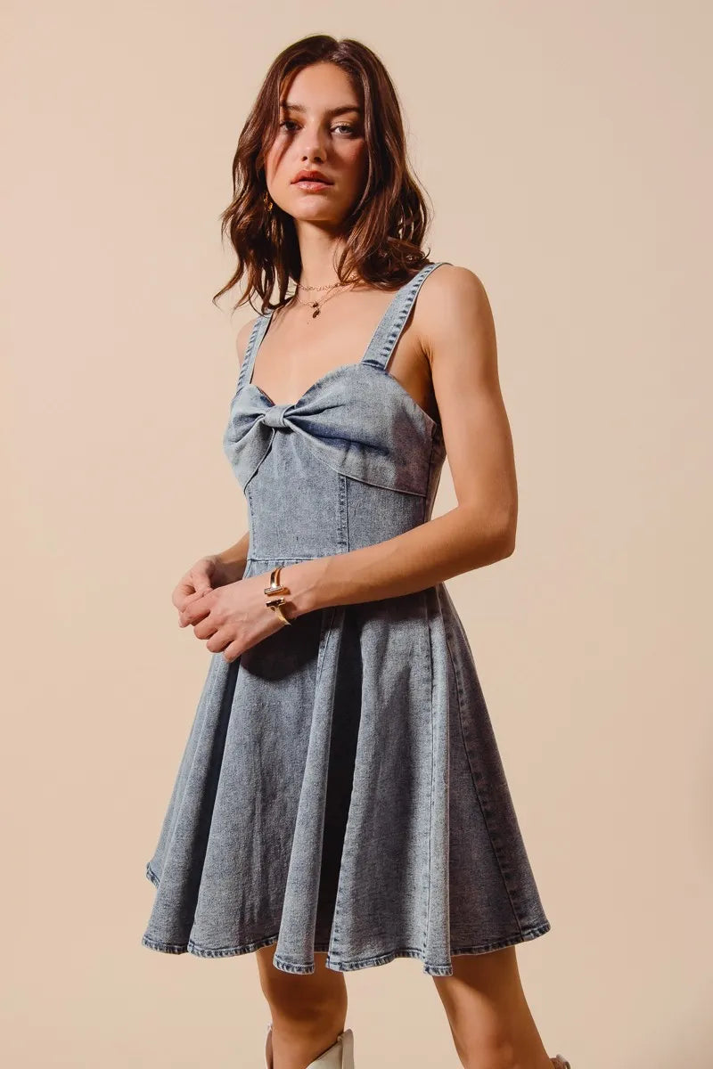 Woman wearing a denim dress with a bow detail on a beige background