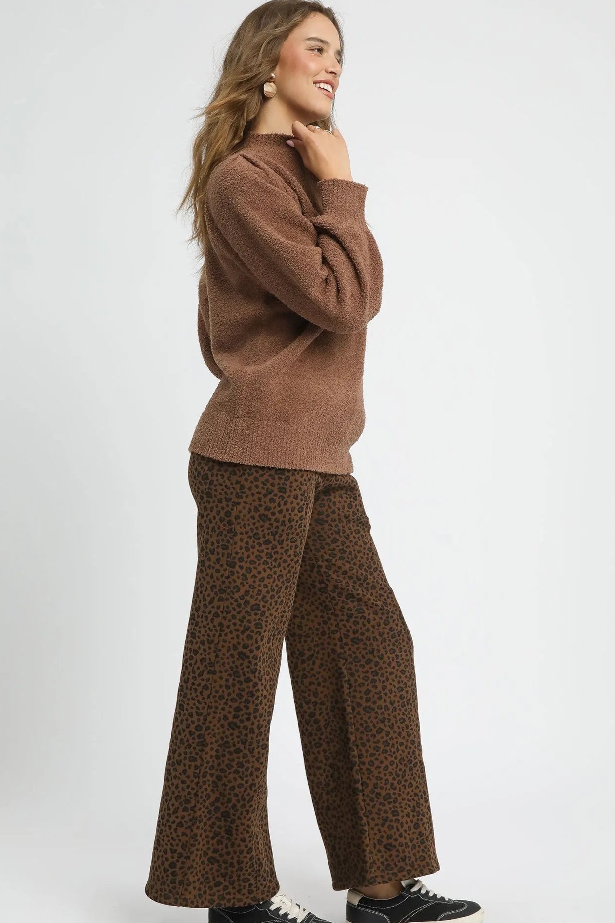 Woman wearing a brown sweater and leopard print pants on a white background