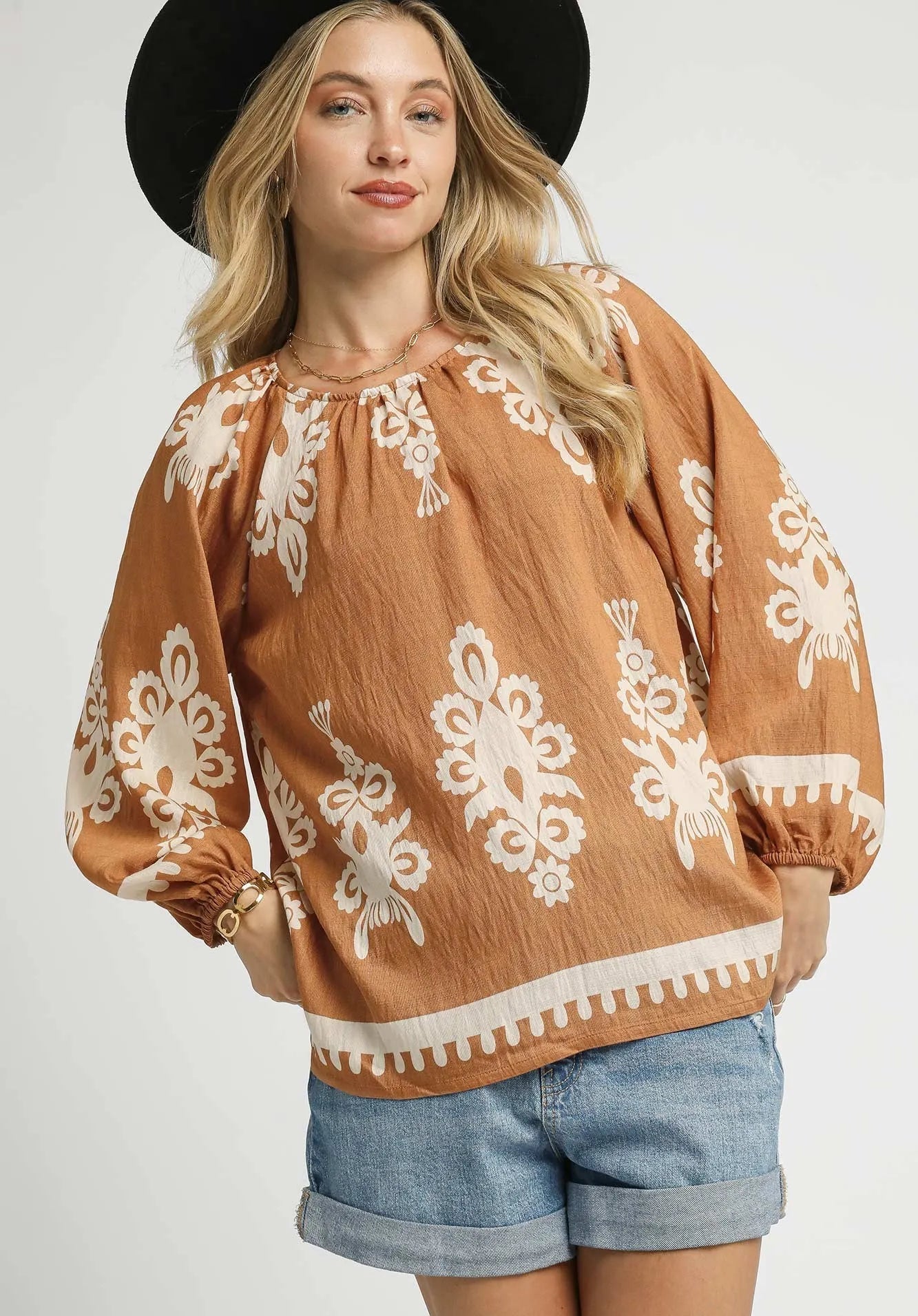 Woman wearing a brown blouse with white lace patterns and denim shorts on a white background