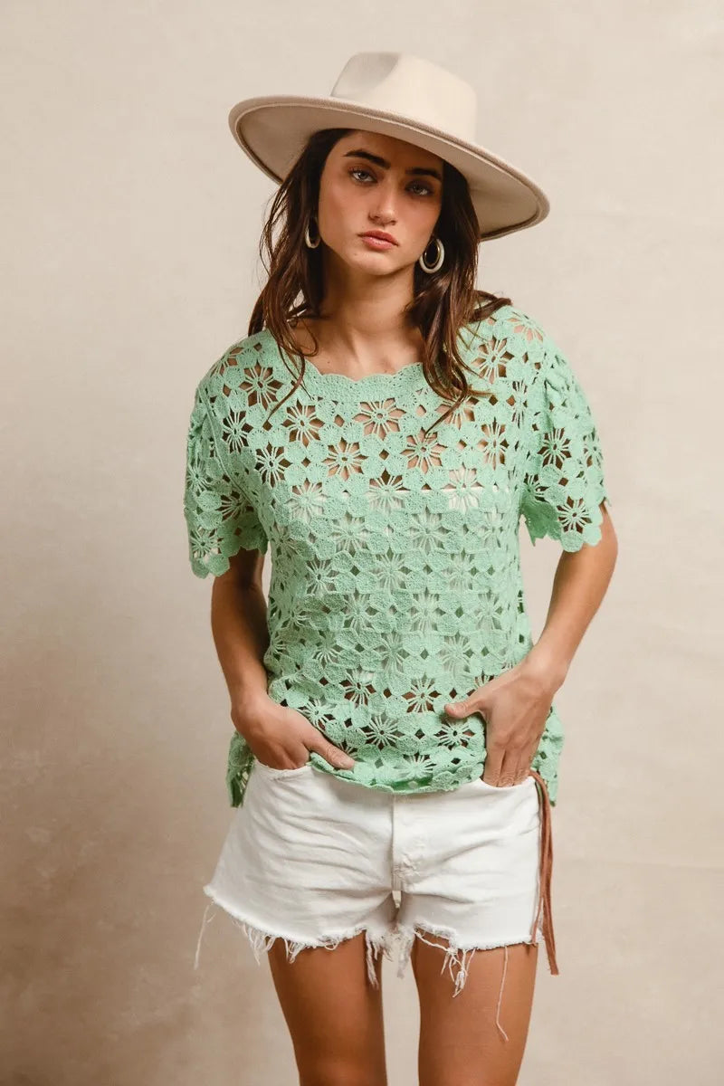 Woman wearing a green floral top and white shorts with a beige hat on a beige background