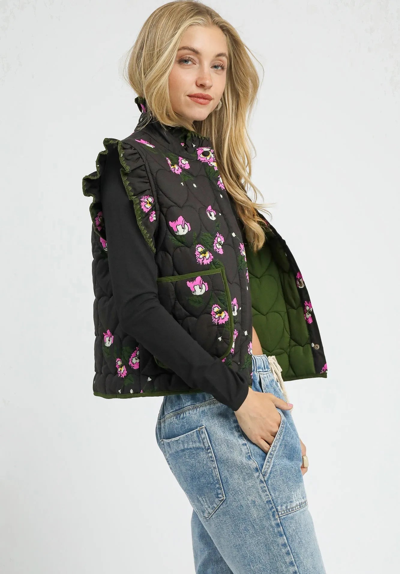 Woman wearing a black floral-patterned vest over a green jacket on a white background