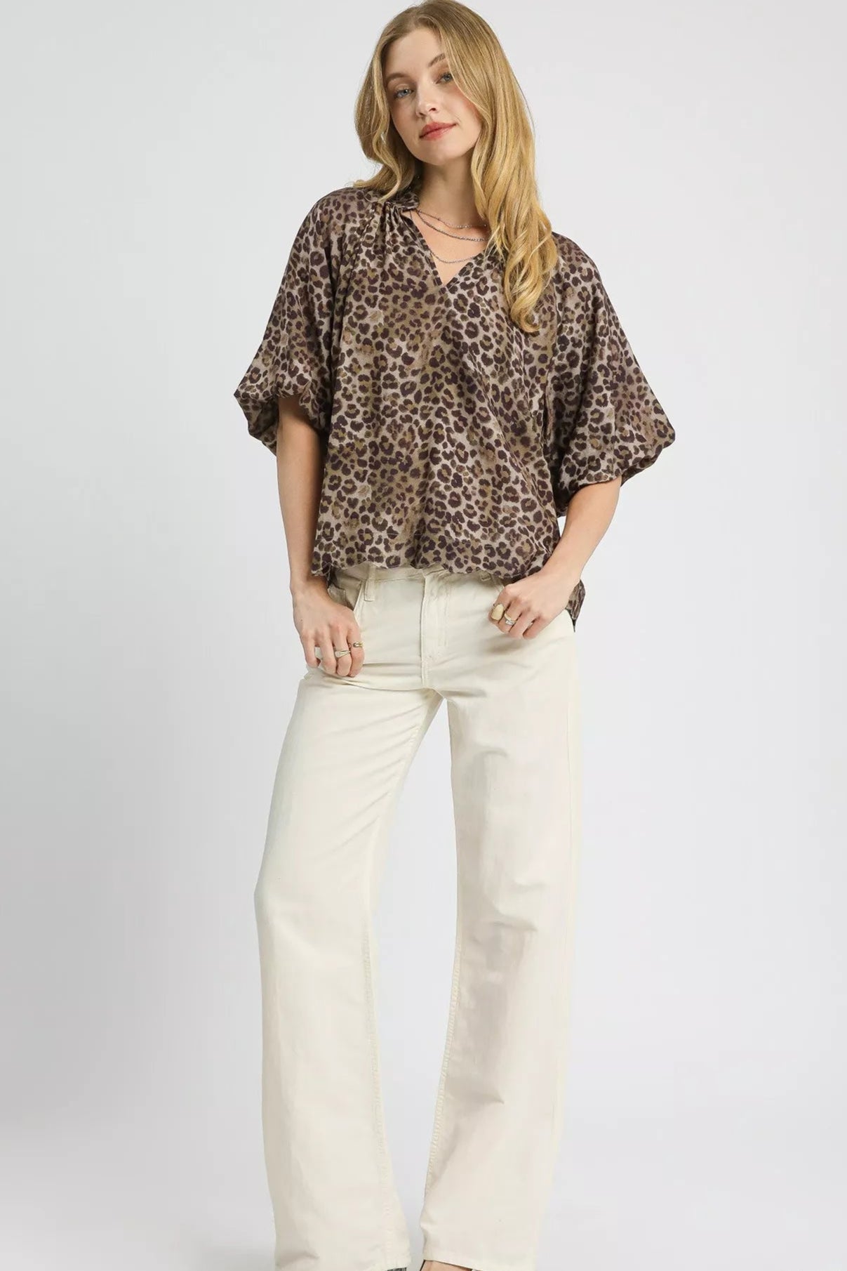 Woman wearing a leopard print top and white pants on a white background