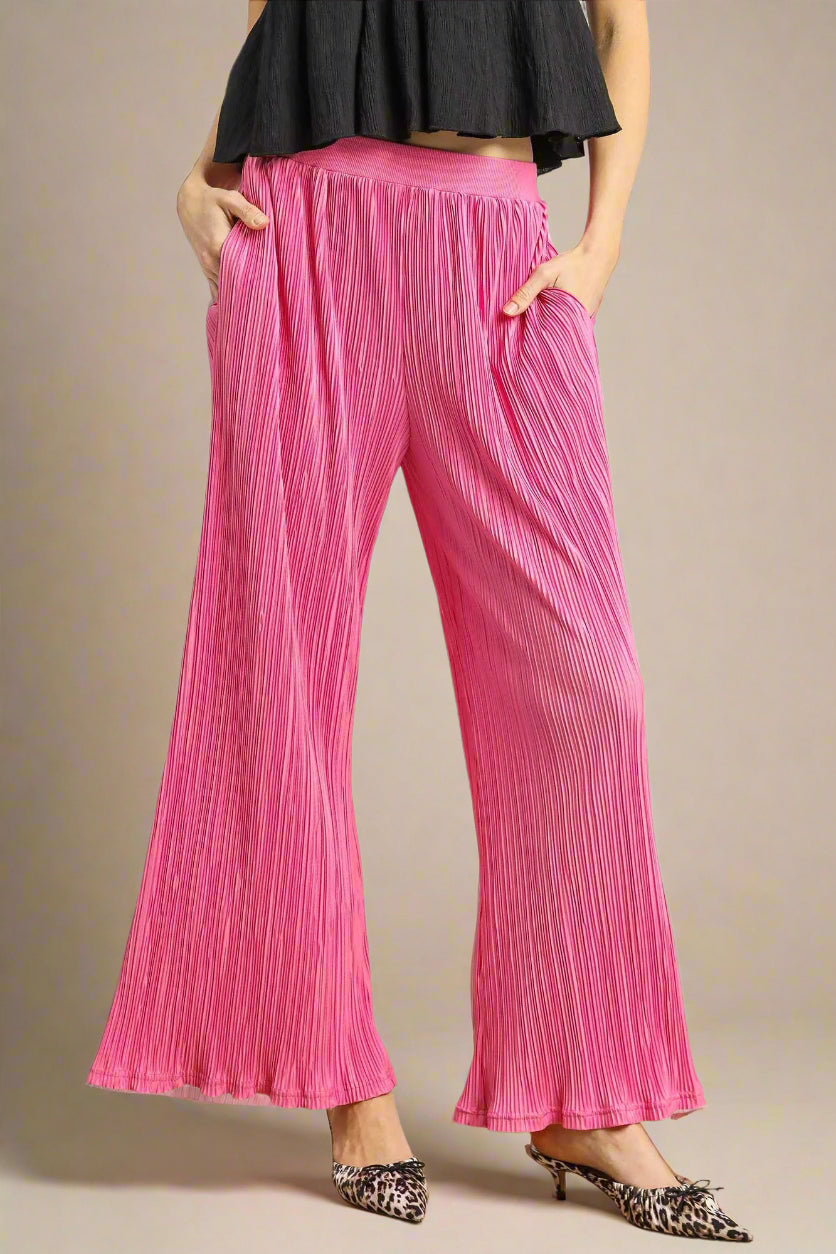Person wearing bright pink pleated pants with a plain background