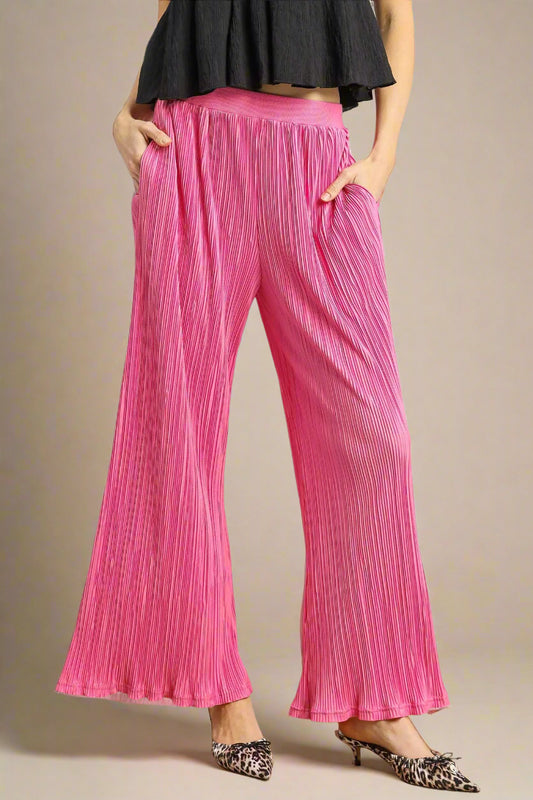 Person wearing bright pink pleated pants with a plain background