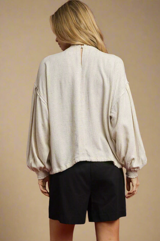 Person wearing a beige blouse with balloon sleeves against a red background