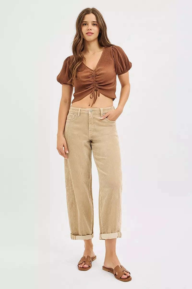 Woman wearing a brown ruched top and beige pants on a white background