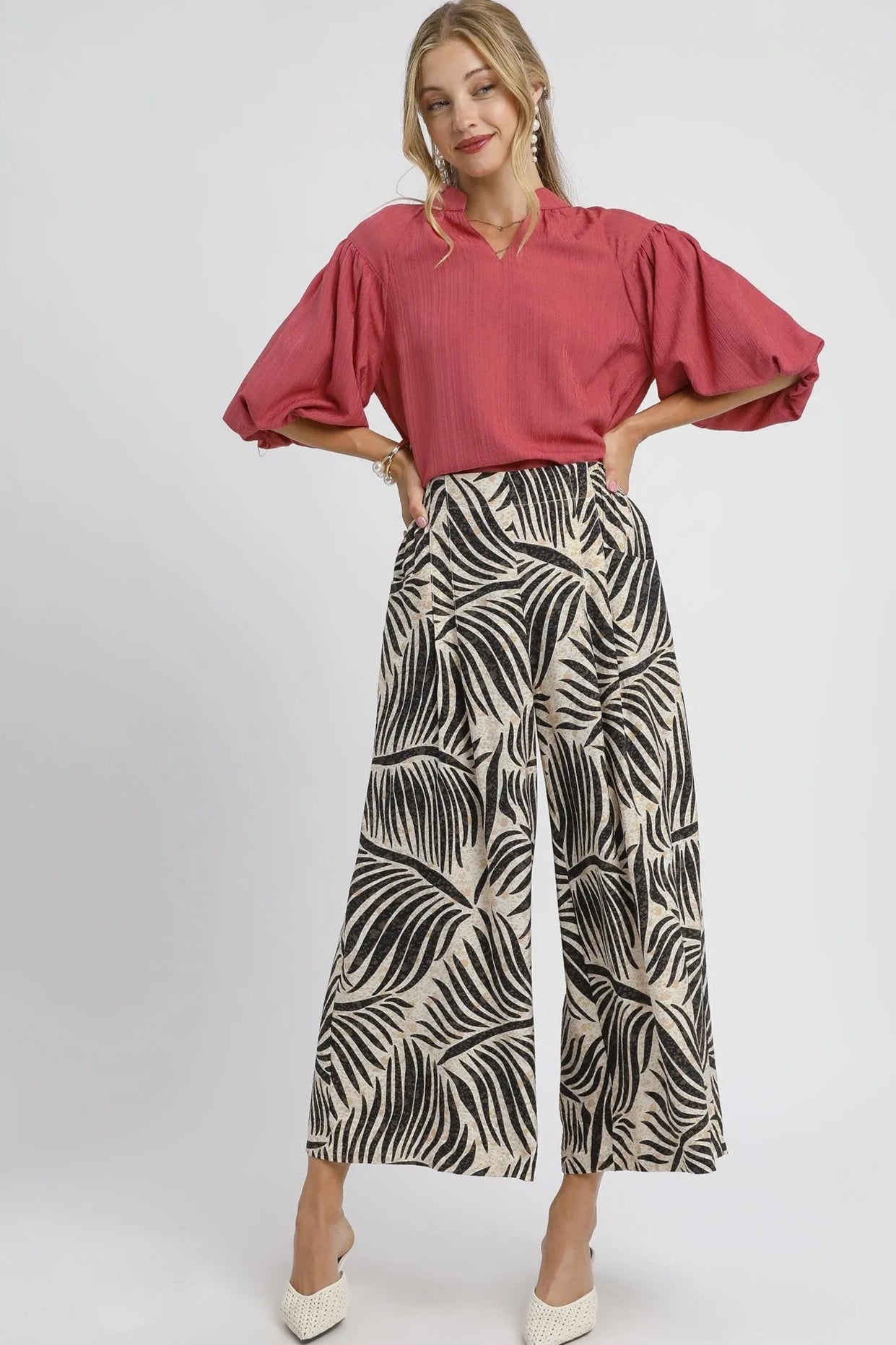 Woman wearing a pink blouse and patterned pants on a white background