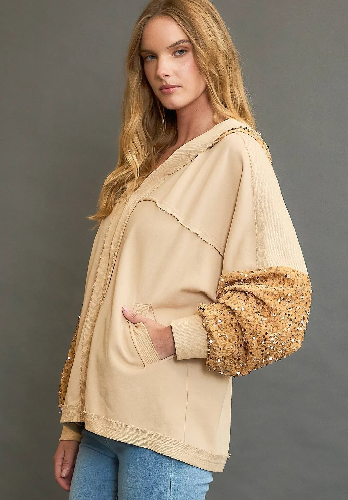 Woman wearing a beige sweater with sequin sleeves against a gray background