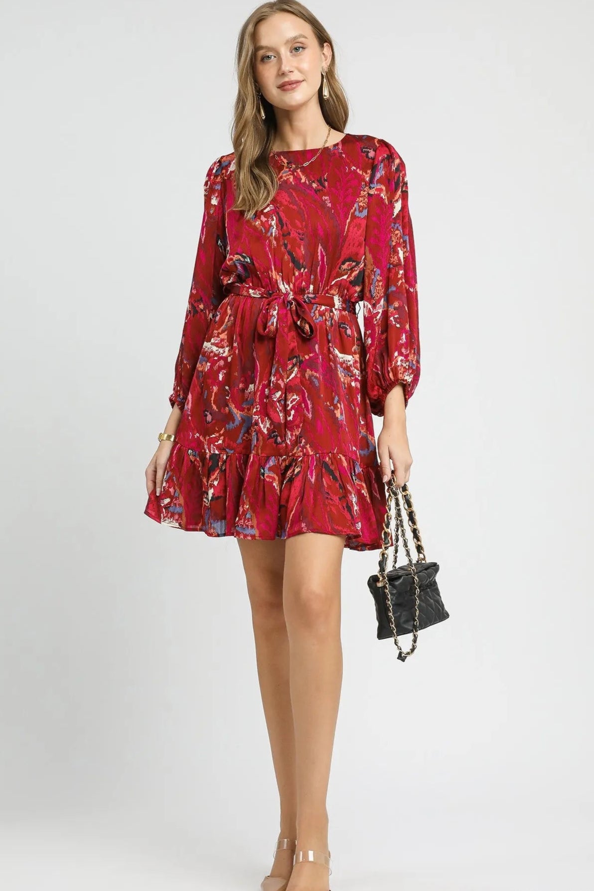 Woman wearing a red floral dress holding a black handbag on a white background