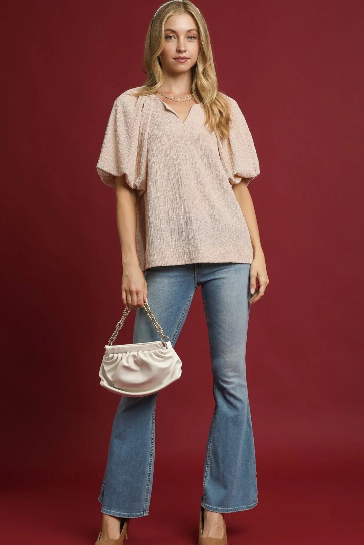 Woman wearing a beige blouse and blue jeans holding a handbag against a red background