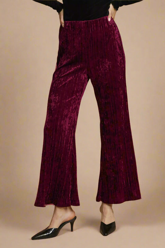 Burgundy velvet pants worn by a person on a beige background