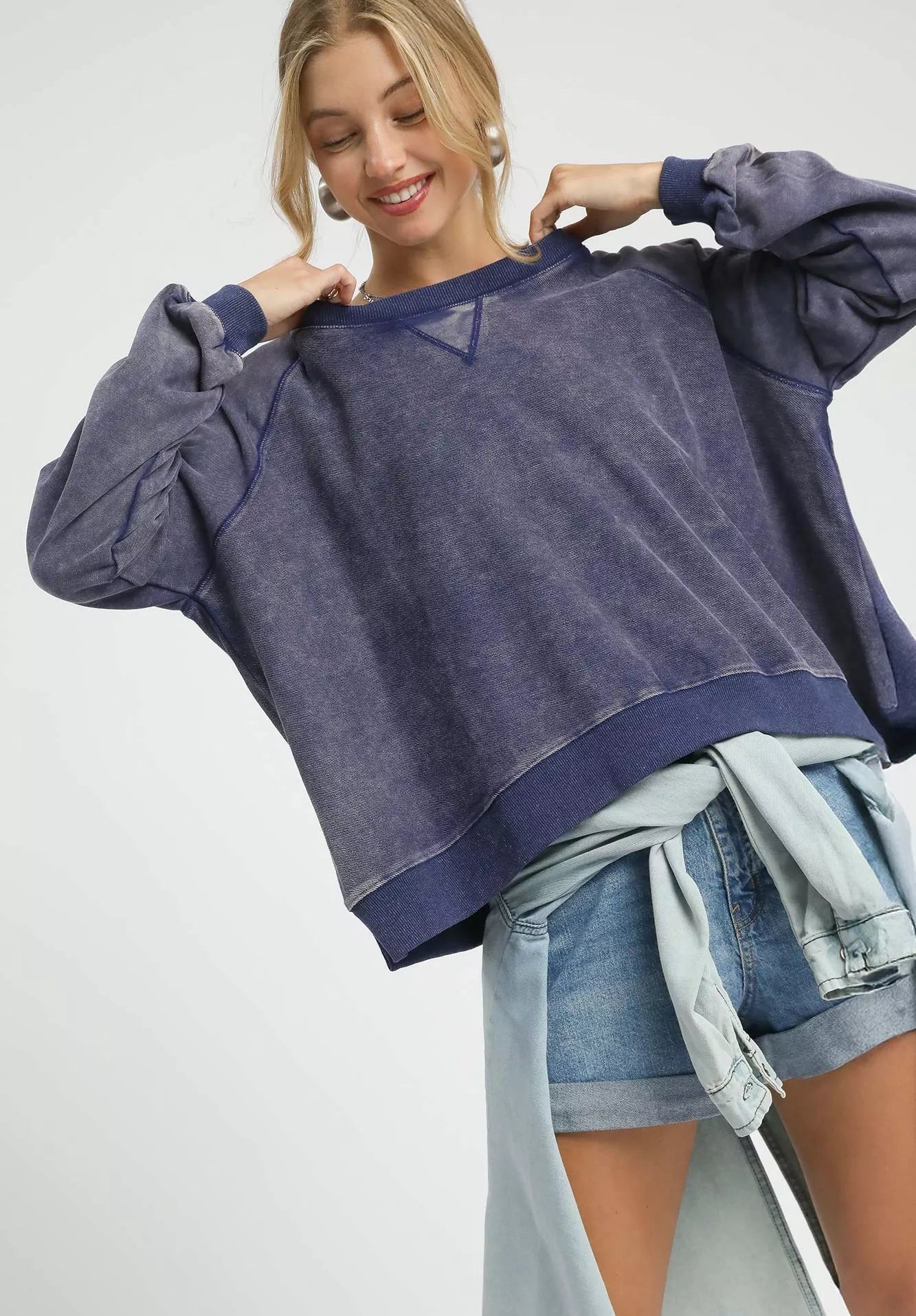 Woman wearing a navy blue sweatshirt with denim shorts on a white background