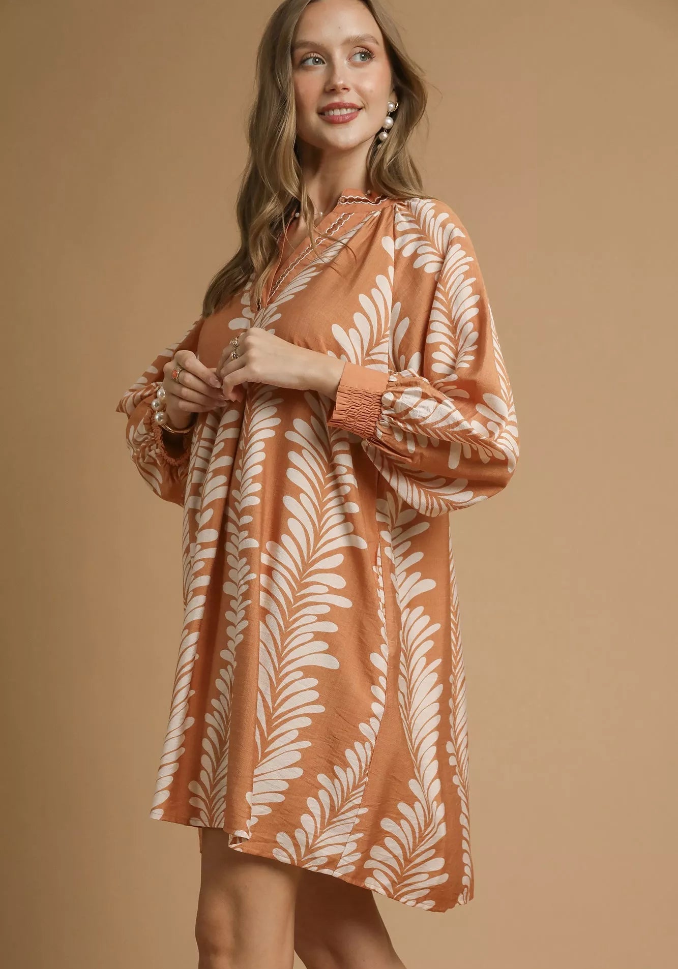 Woman wearing a taupe dress with white leaf pattern on a beige background