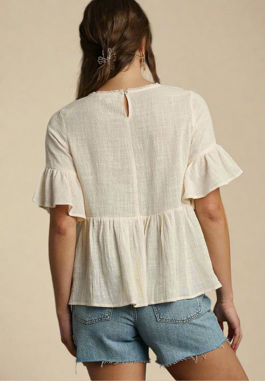 Woman wearing a cream blouse with ruffled sleeves and denim shorts on a beige background