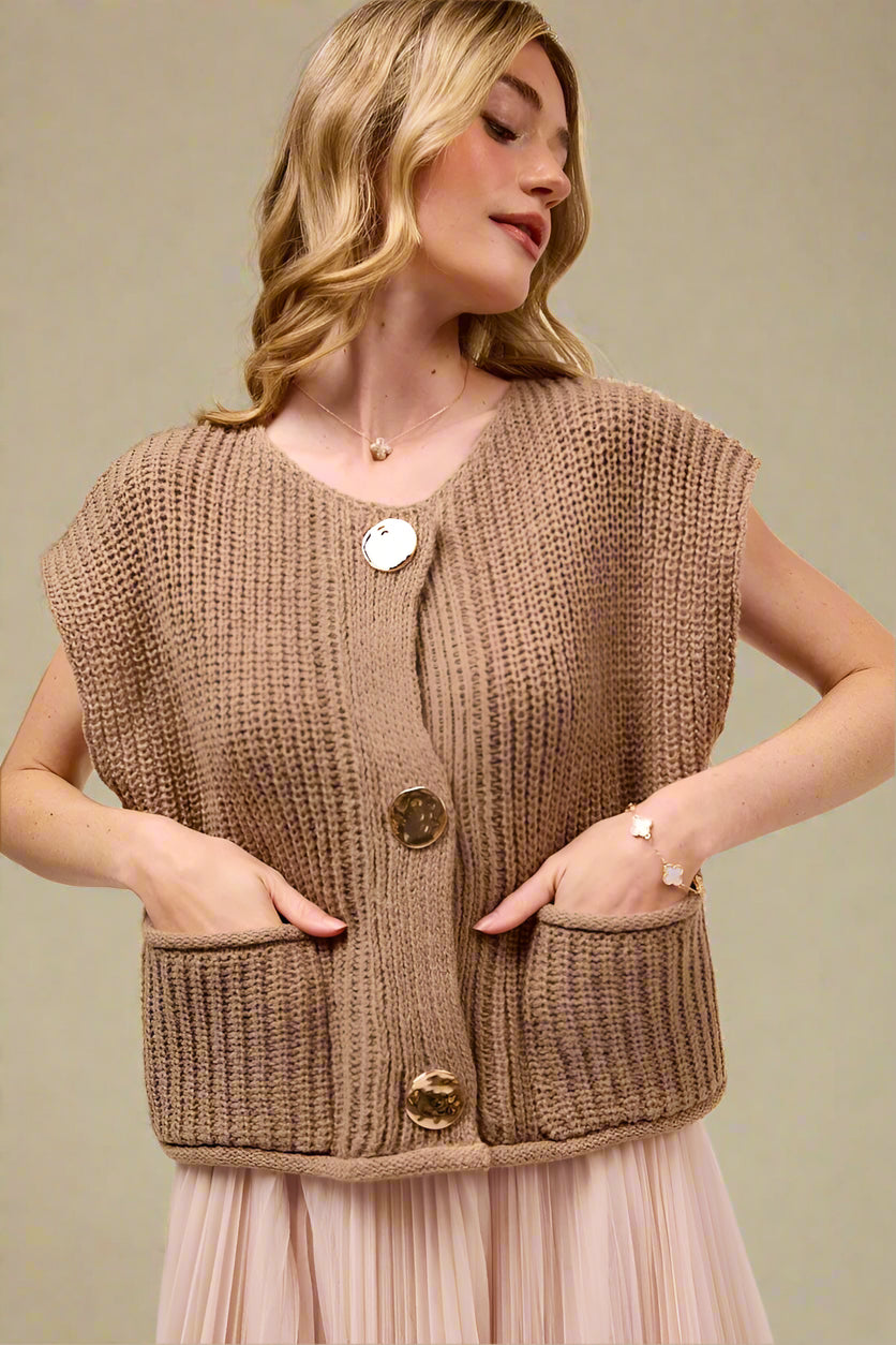 Woman wearing a brown knitted vest with gold buttons on a beige background
