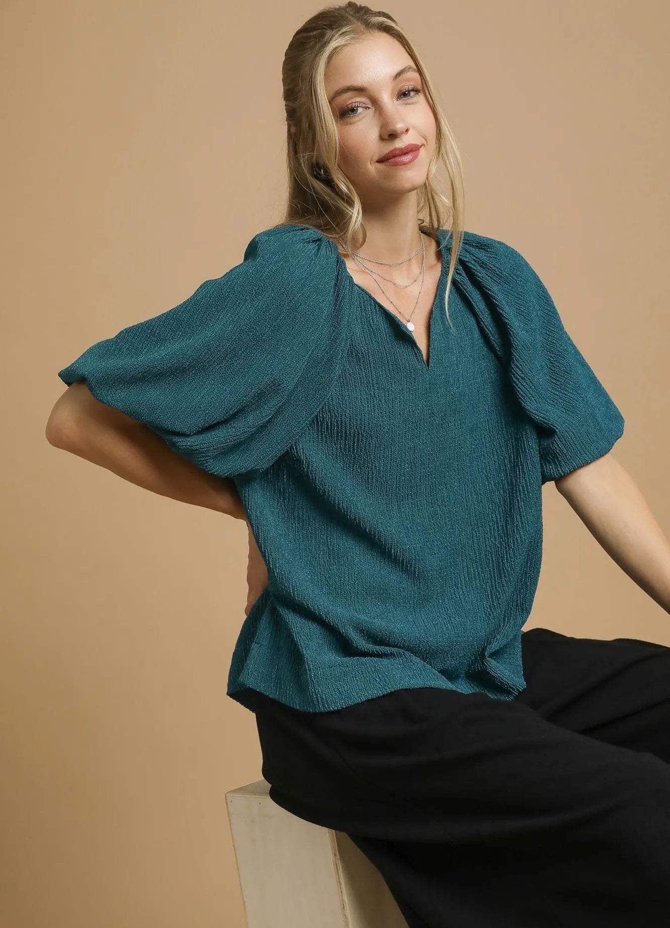 Woman wearing a teal blouse with puffed sleeves against a beige background