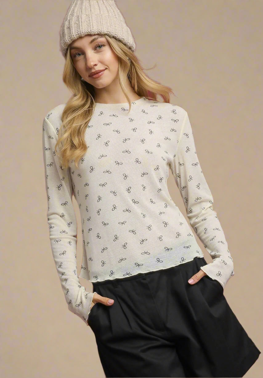 Woman wearing a cream long-sleeve top with a subtle pattern and black pants against a beige background.