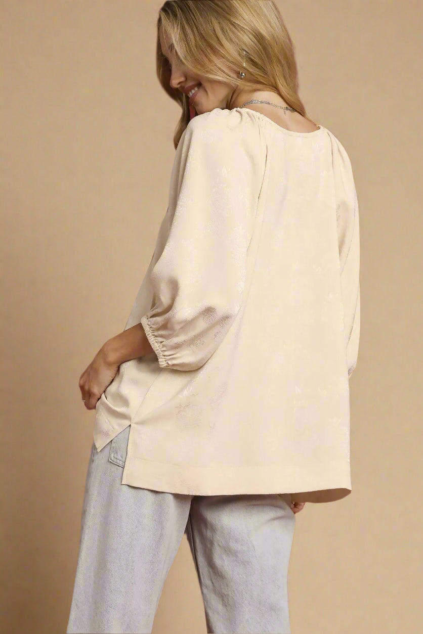 Woman wearing a beige blouse and light gray pants against a beige background