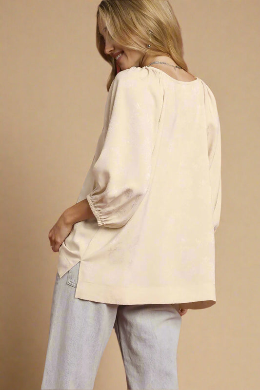 Woman wearing a beige blouse and light gray pants against a beige background