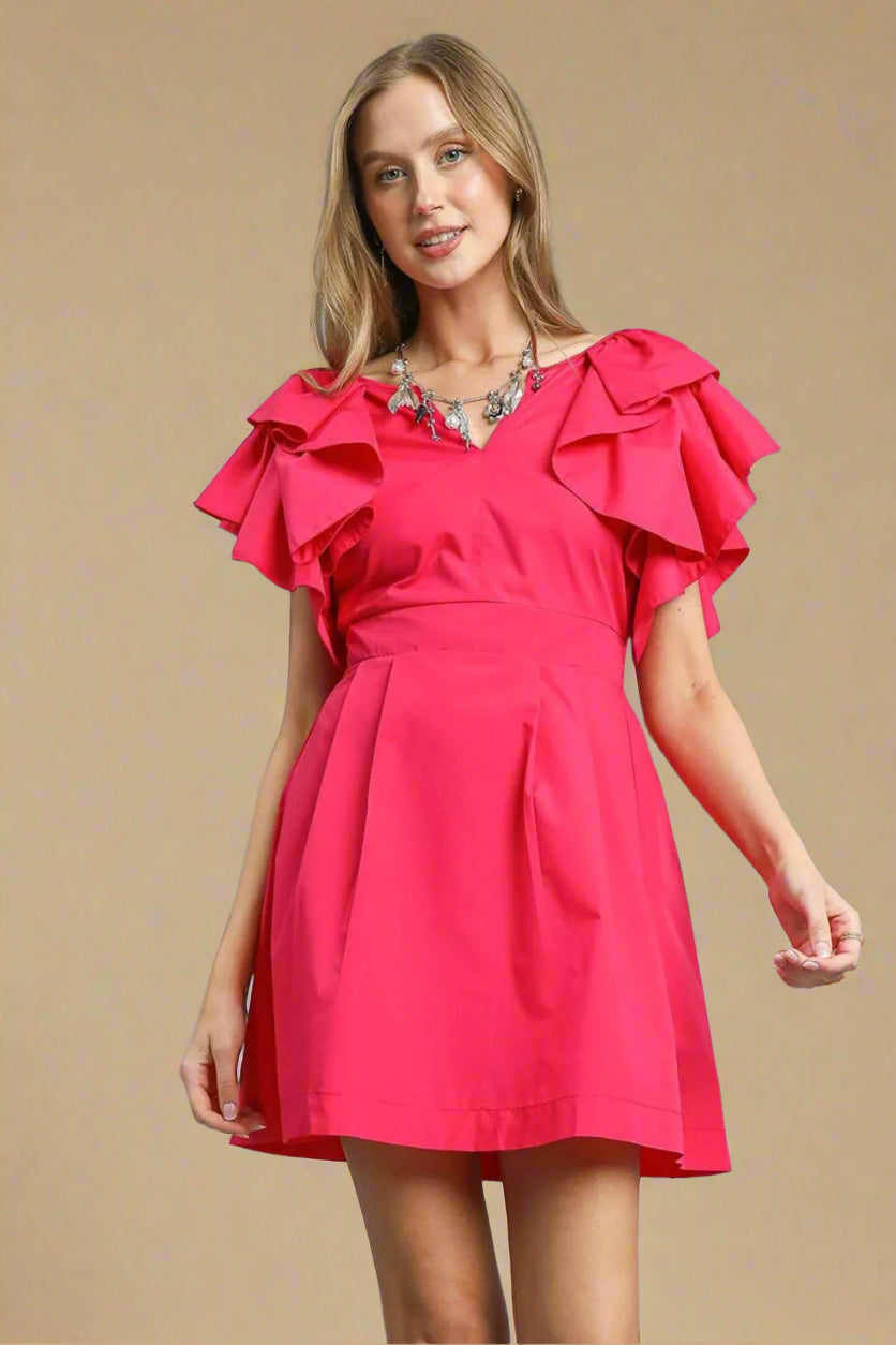 Woman wearing a bright pink dress with ruffled sleeves on a beige background