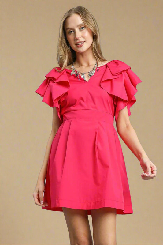 Woman wearing a bright pink dress with ruffled sleeves on a beige background